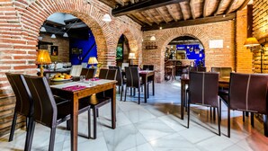 Un restaurante con arcos de ladrillo, vigas de madera e iluminación moderna. Mesas y sillas dispuestas para comer.