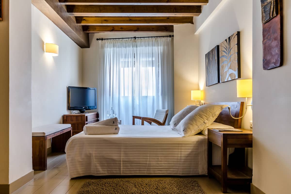 Una habitación de hotel con cama, mesita de noche, televisor y una obra de arte en la pared.