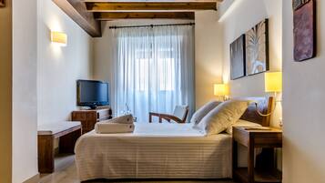 A hotel room with a bed, bedside table, TV, and artwork on the wall.