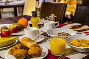 A breakfast table with various food items, including fruits, muffins, and cereal.