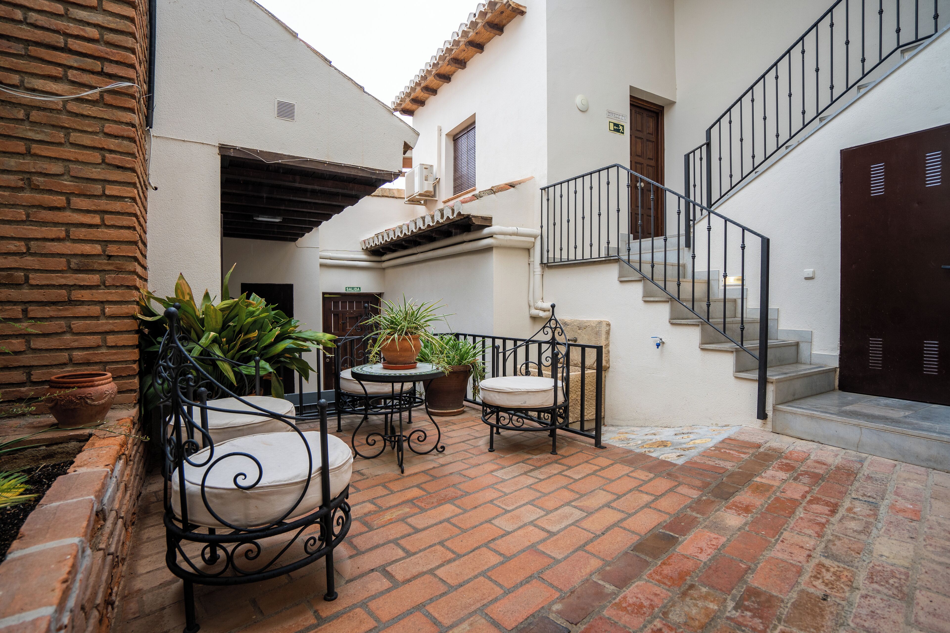 Un patio con suelo de ladrillo, mobiliario exterior, plantas en macetas y una escalera.