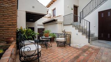 Un patio con suelo de ladrillo, mobiliario exterior, plantas en macetas y una escalera.