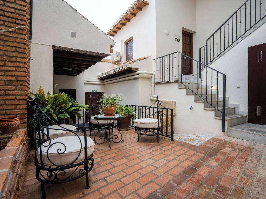 Un patio con suelo de ladrillo, mobiliario exterior, plantas en macetas y una escalera.