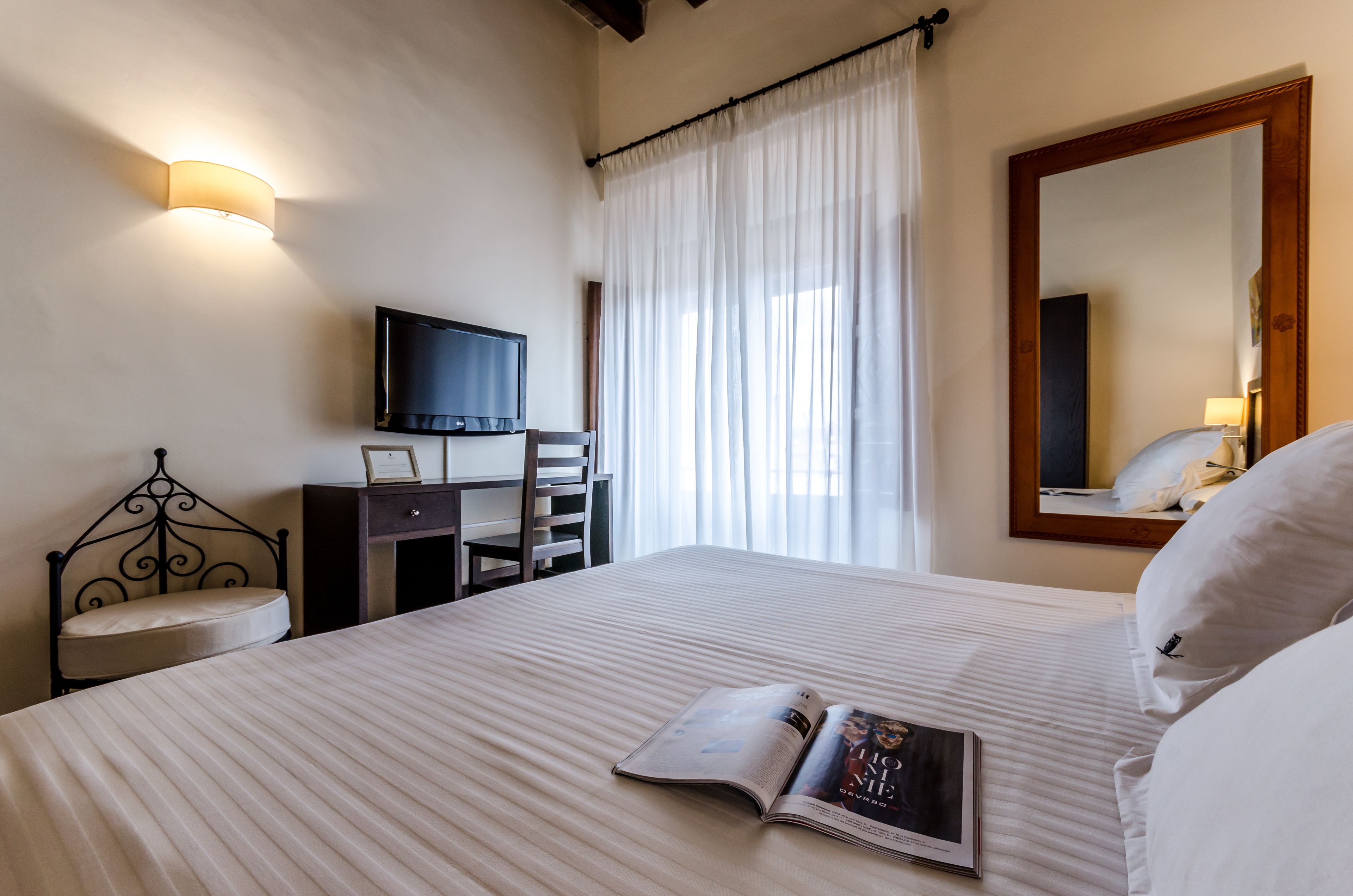 A hotel room with a bed, a desk, a chair, a television, and a large mirror.