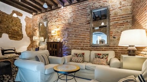 Una sala de estar acogedora con pared de ladrillo, sofás blancos, una mesa de centro redonda y una lámpara.