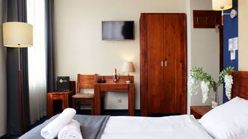 Una habitación de hotel con cama, escritorio, televisión, armario y mesita de noche con lámpara.