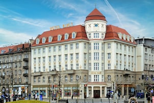 A large, historic building with the sign "HOTEL PIAST" indicating it is a hotel. It features multiple floors with a classic architectural style, including a prominent dome and a red roof.