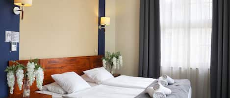 A hotel room with two beds, a wooden headboard, white bedding, a vase with white flowers, and a window with curtains.