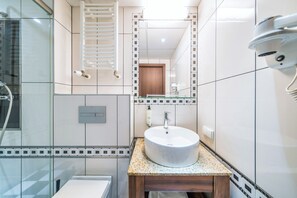 A modern bathroom with a glass shower enclosure, a white sink with a wooden vanity, and a mirror with a decorative frame.