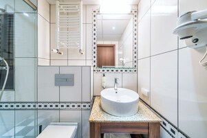 A modern bathroom with a glass shower enclosure, a white sink with a wooden vanity, and a mirror with a decorative frame.