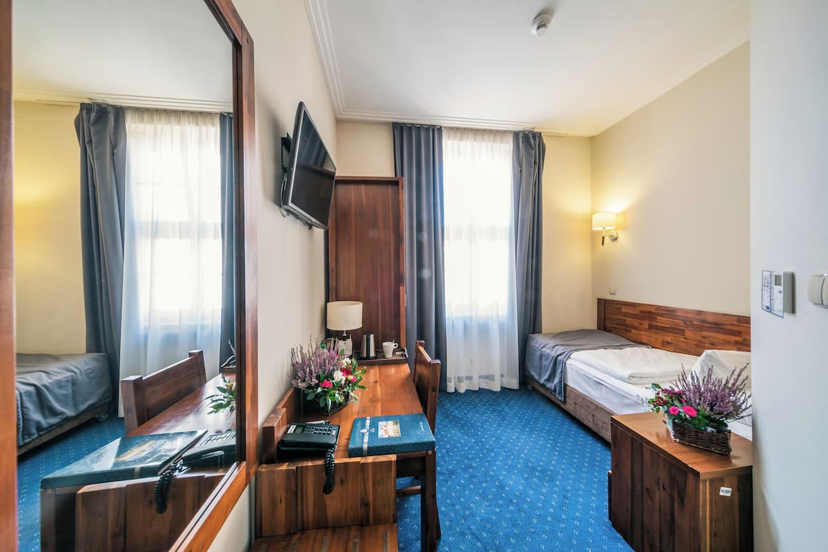 A hotel room with a wooden desk, a bed, a TV, and a window with curtains.