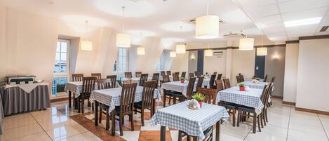 A spacious dining area with multiple tables and chairs, air conditioning units, and pendant lights.