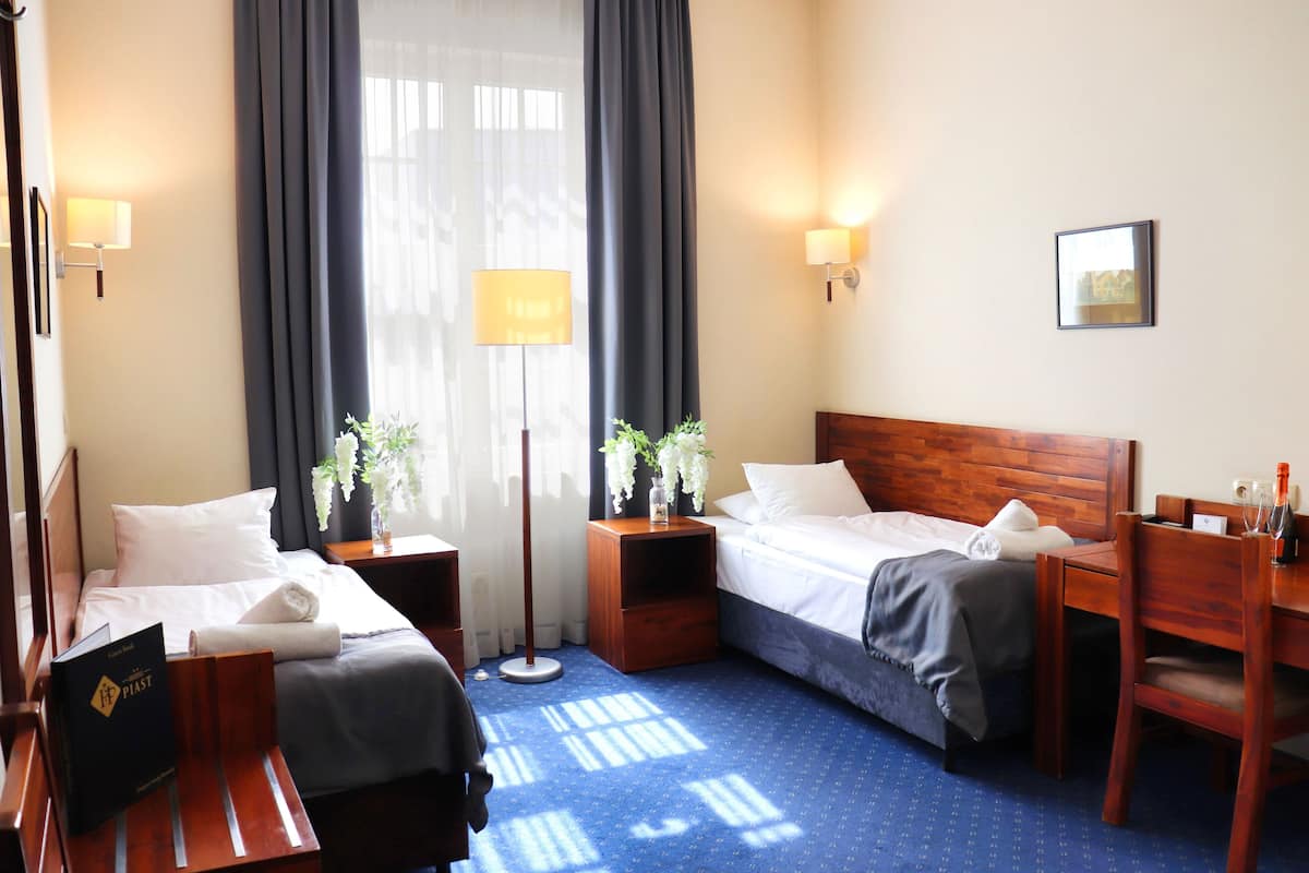 A hotel room with two beds, a desk, a chair, a lamp, and a picture on the wall.