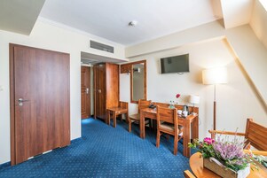 Ett hotellrum med ett skrivbord i trä, en stol, en spegel, en tv som är monterad på väggen och en lampa.