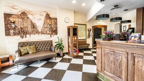 Un hall de hotel con suelo a cuadros, una recepción, un sofá, un reloj y un mural grande en la pared.