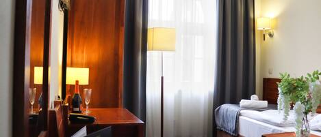 A hotel room with a bed, a desk with a lamp, a mirror, and a window with curtains.