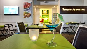 Un restaurante con una mesa verde, una copa de cóctel y una pantalla de televisión.