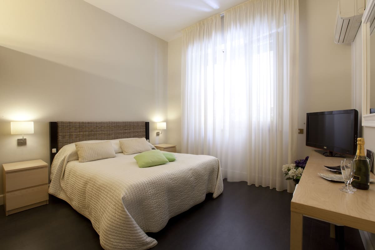 Ein Hotelzimmer mit Bett, Nachttischen, einem Fernseher, einer Champagnerflasche und einer Blumenkomposition.
