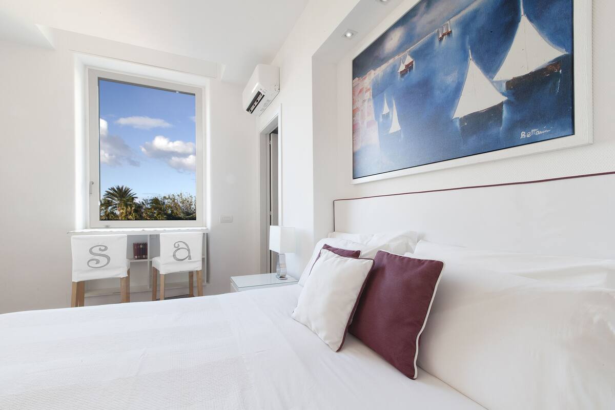 Ein Hotelzimmer mit einem großen Bett, einem Schreibtisch mit Stühlen, einem Fenster mit Blick und einem Bild an der Wand.