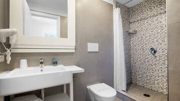 A bathroom with a white sink, a toilet, a shower with a tiled wall, and a mirror above the sink.