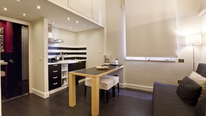 Cocina compacta con comedor, sofá y ventana con persianas.