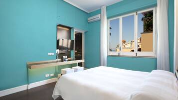 A hotel room with teal walls, a large bed, a built-in TV, and a window with a view of buildings.