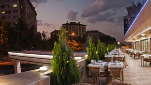 An outdoor dining area with tables and chairs, surrounded by greenery and buildings in the background. - Dundar Hotel (Konya)