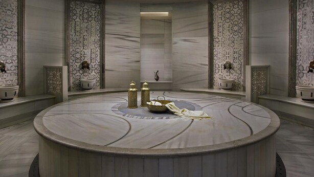 A circular marble-tiled bathroom with ornate wall panels, a central sink, and two wall-mounted light fixtures. - Dundar Hotel (Konya)