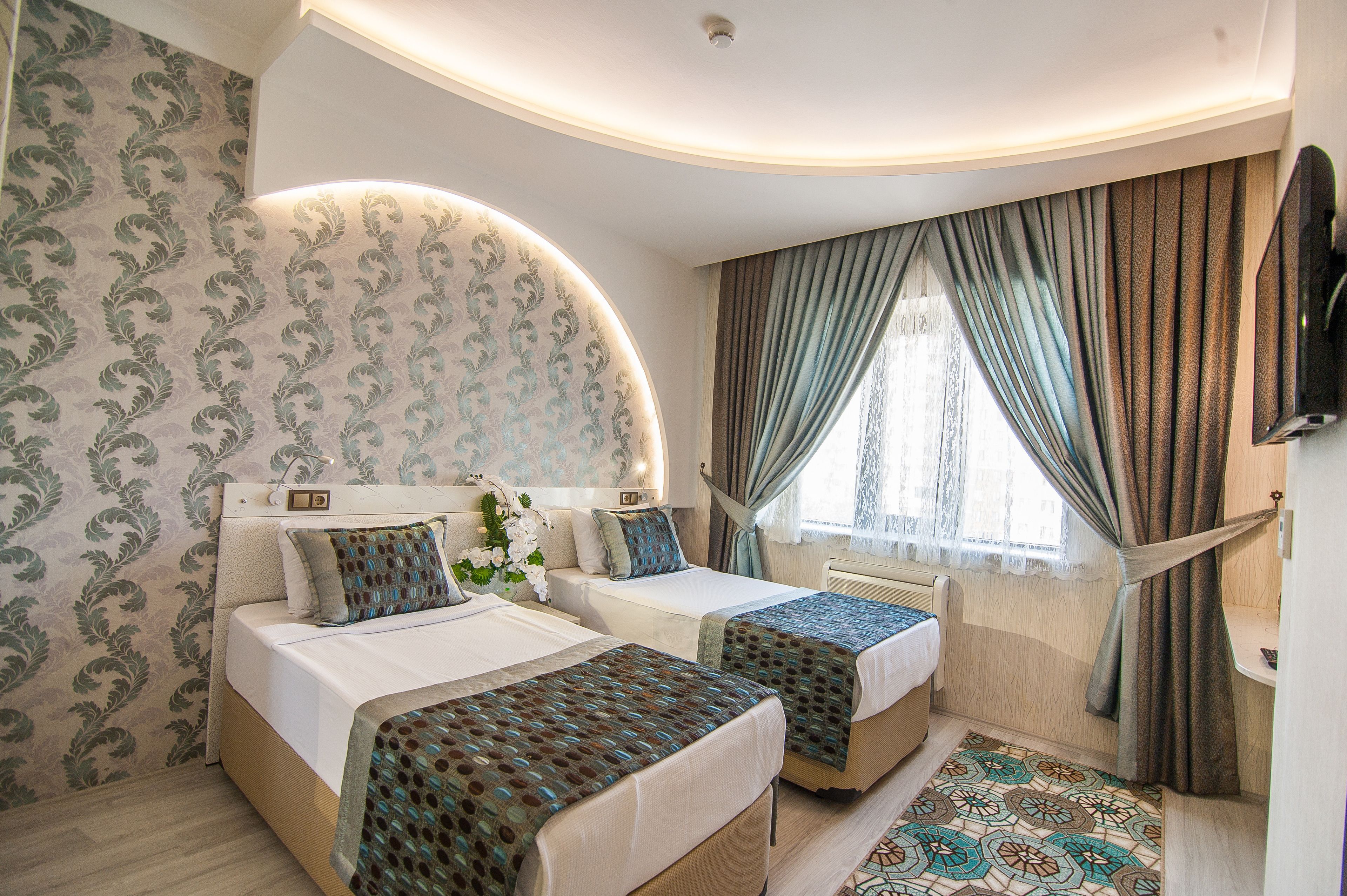 A hotel room with two beds, a curved ceiling, a large window with curtains, and a patterned rug.