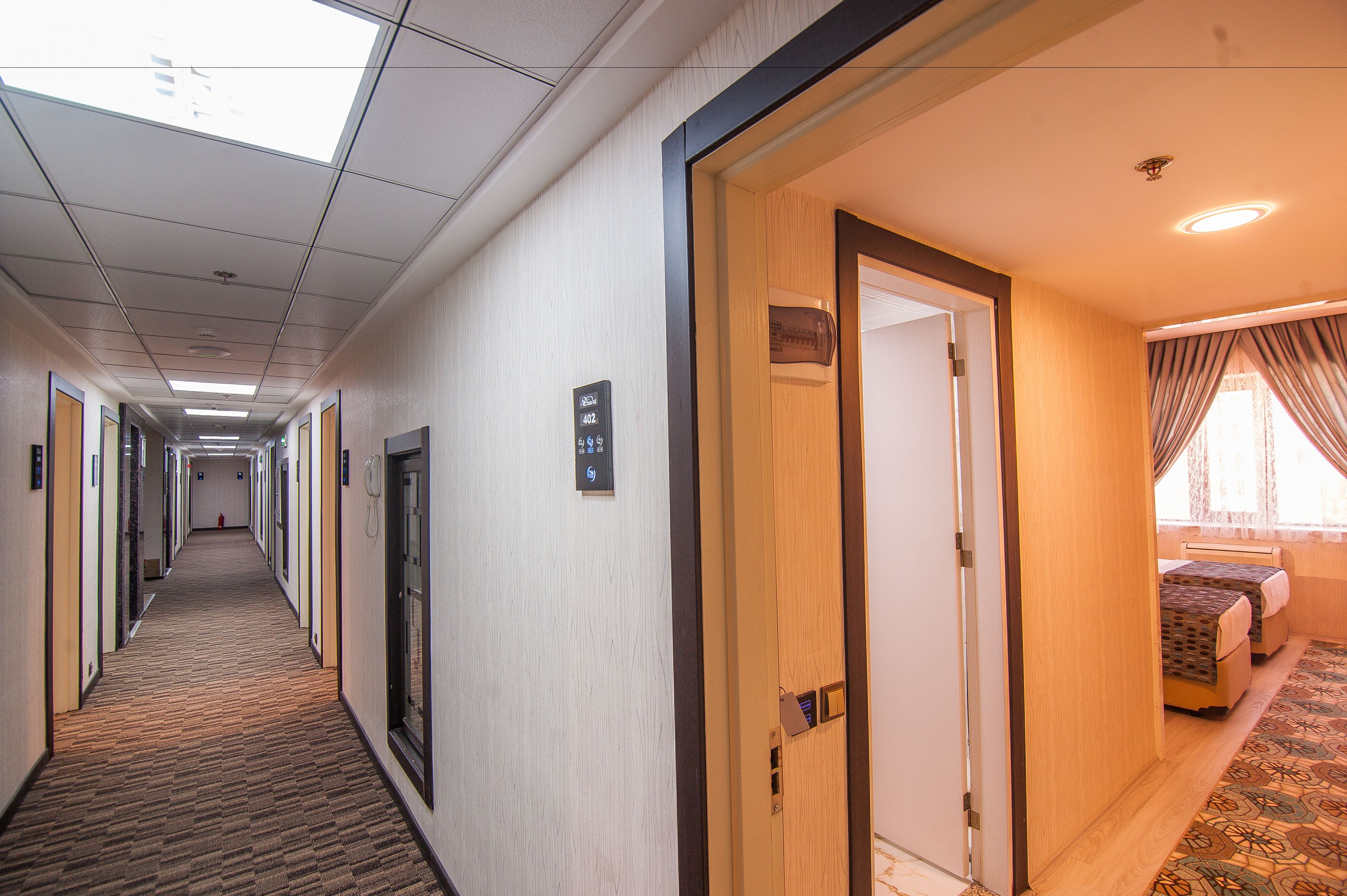 A hotel hallway with carpeted floors, wooden doors, and a bed with a patterned bedspread in a room.