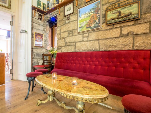 A cozy room with a red velvet sofa, a marble table, and a stone wall with framed pictures. - Cumberland Hotel (Edinburgh)