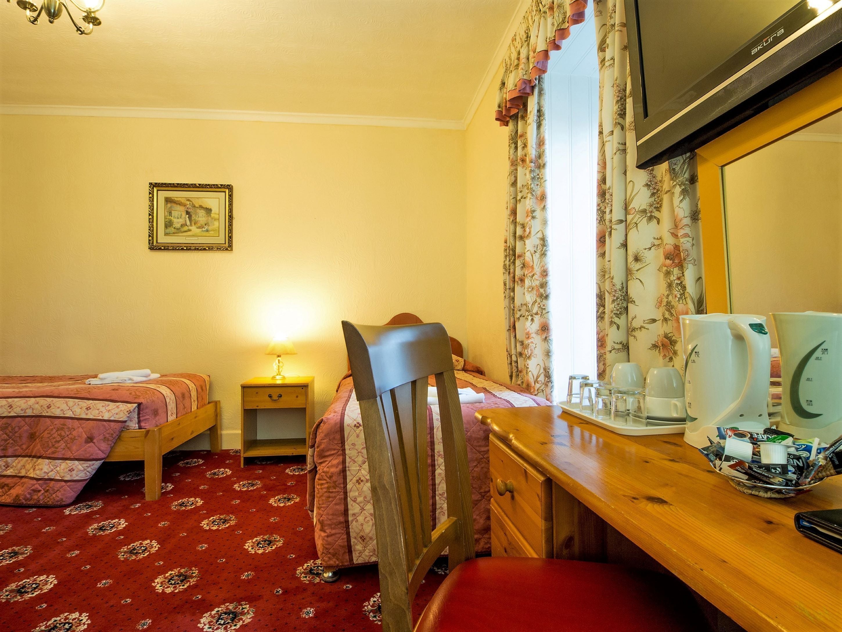A hotel room with two beds, a desk with a chair, a television, and a coffee station.