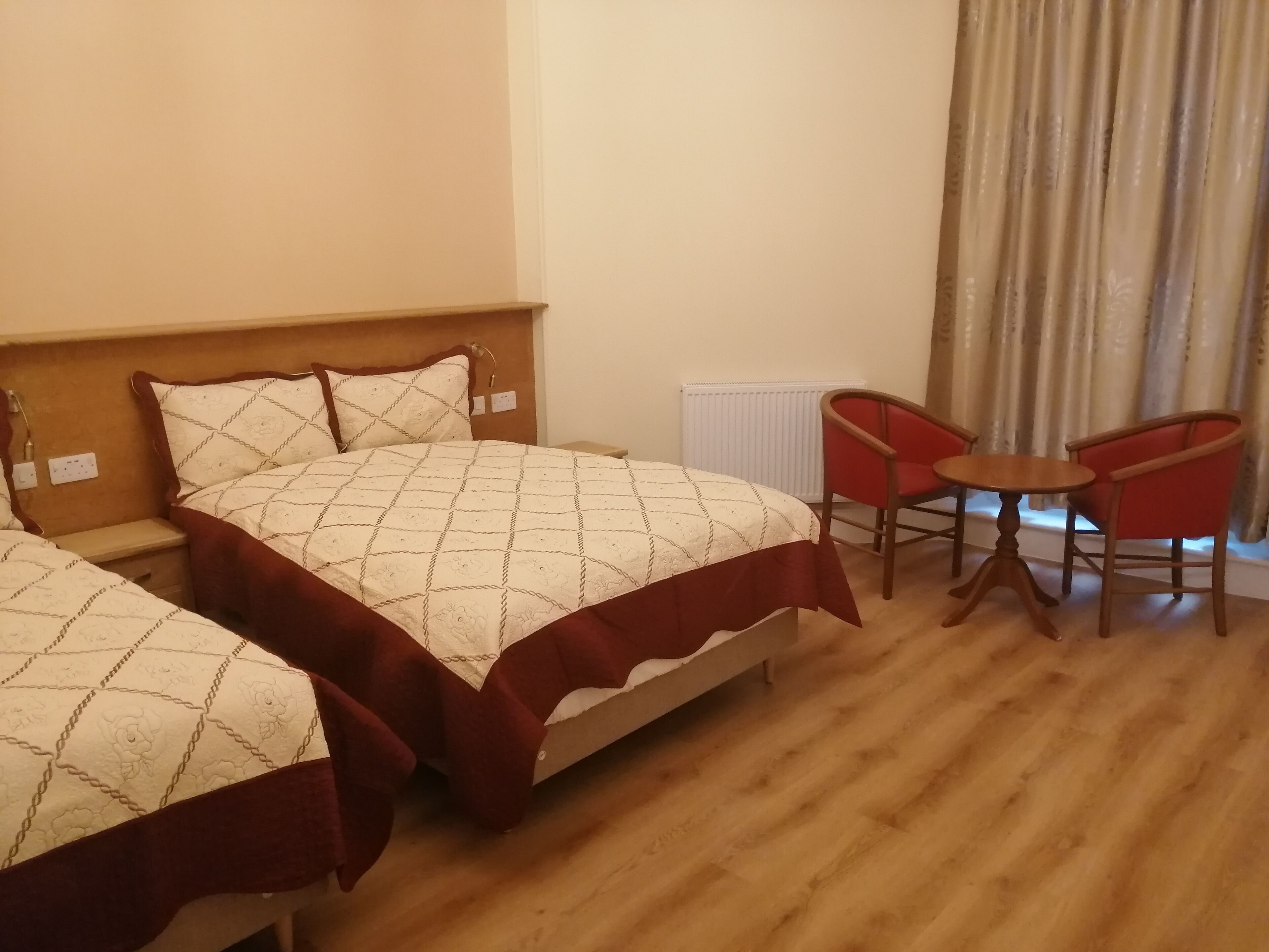 A hotel room with two beds, a small table, and two red chairs.