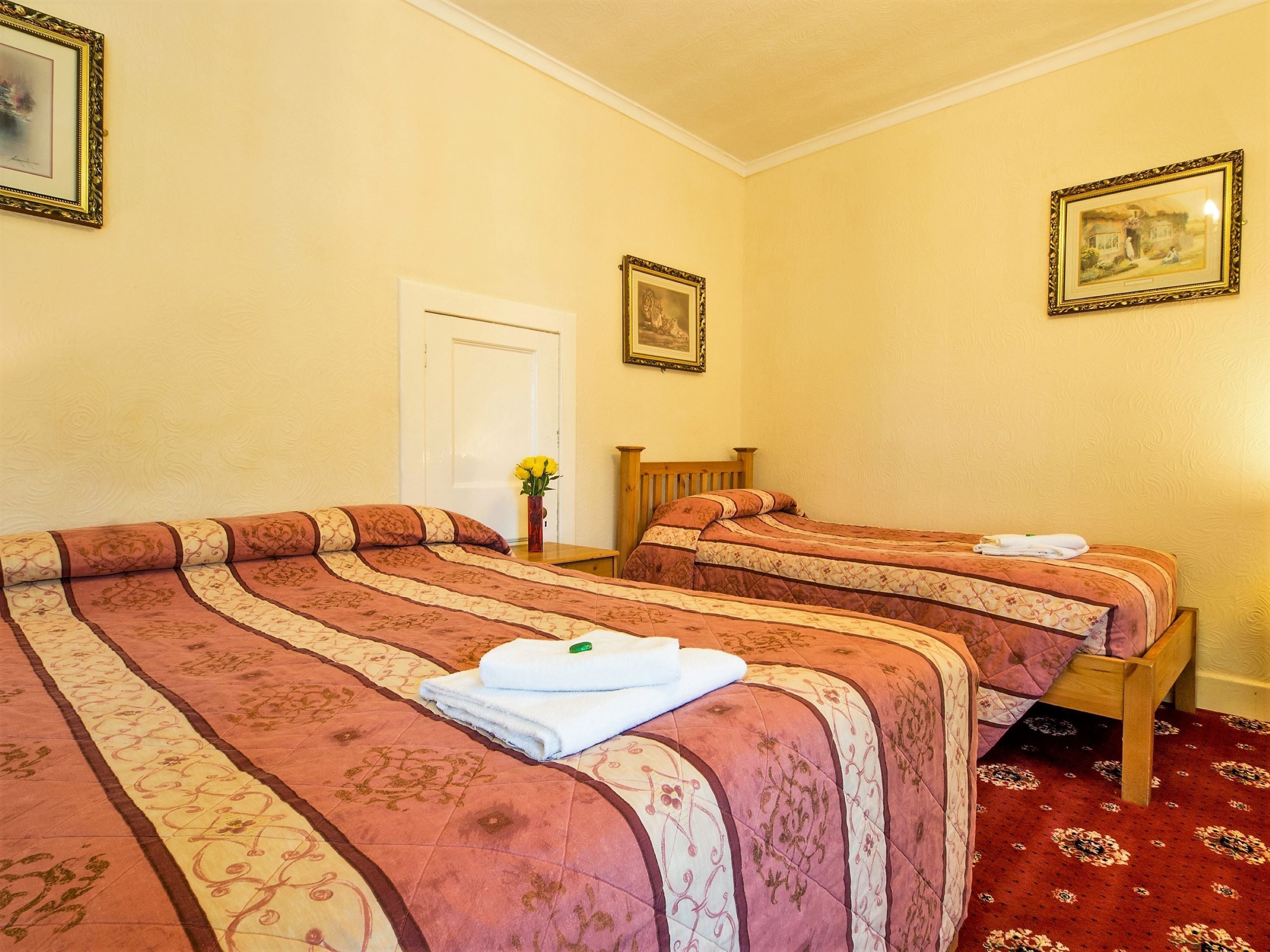 Une chambre d’hôtel avec deux lits, une tête de lit en bois, une porte et un tableau encadré au mur.