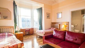 A hotel room with a bed, a red leather sofa, a wooden table, a desk, and a window with curtains. - Corstorphine Lodge (Edinburgh)