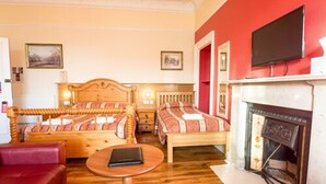 A room with two wooden beds, a red sofa, a small round table, a fireplace, and a television mounted above it. - Corstorphine Lodge (Edinburgh)