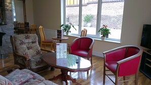 A cozy living room with a fireplace, wooden furniture, and large windows offering a view of the outside. - Corstorphine Lodge (Edinburgh)