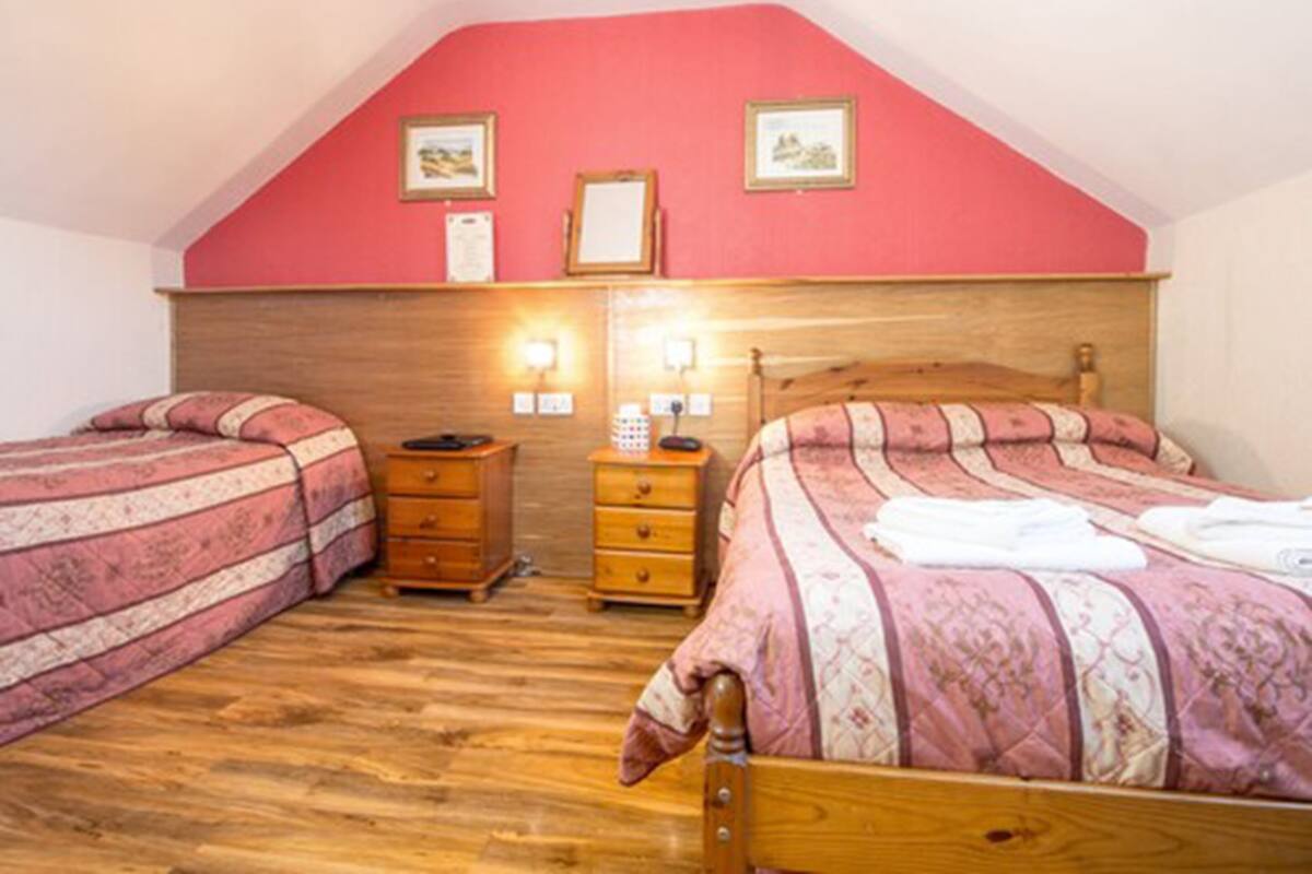 A bedroom with two beds, wooden headboards, a wooden dresser, and a red wall with framed pictures.