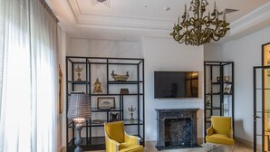 Un salón espacioso con un sofá moderno, dos sillones amarillos, una chimenea y una araña.