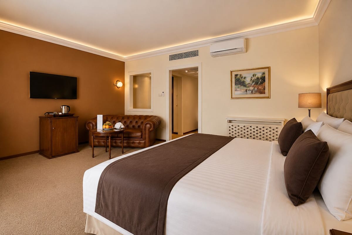 Una habitación de hotel con cama, televisor, escritorio con silla, cafetera y un cuadro en la pared.