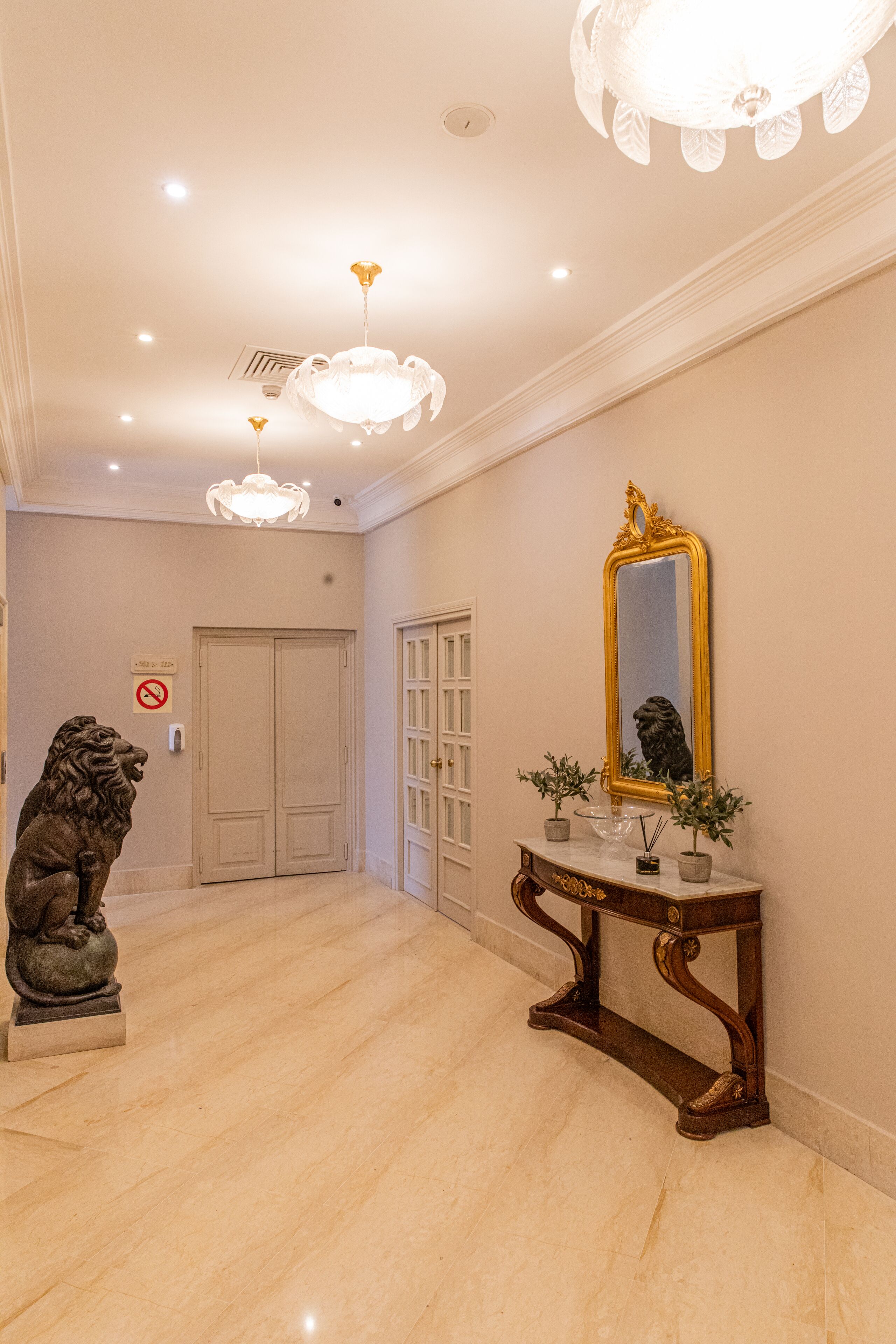 Un couloir doté d’un sol en marbre, d’une statue, d’un miroir et d’une console sur laquelle sont disposées des plantes en pot.