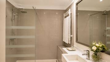 A modern bathroom with a glass-enclosed shower, a large mirror, and a vanity with a sink and a vase of flowers.