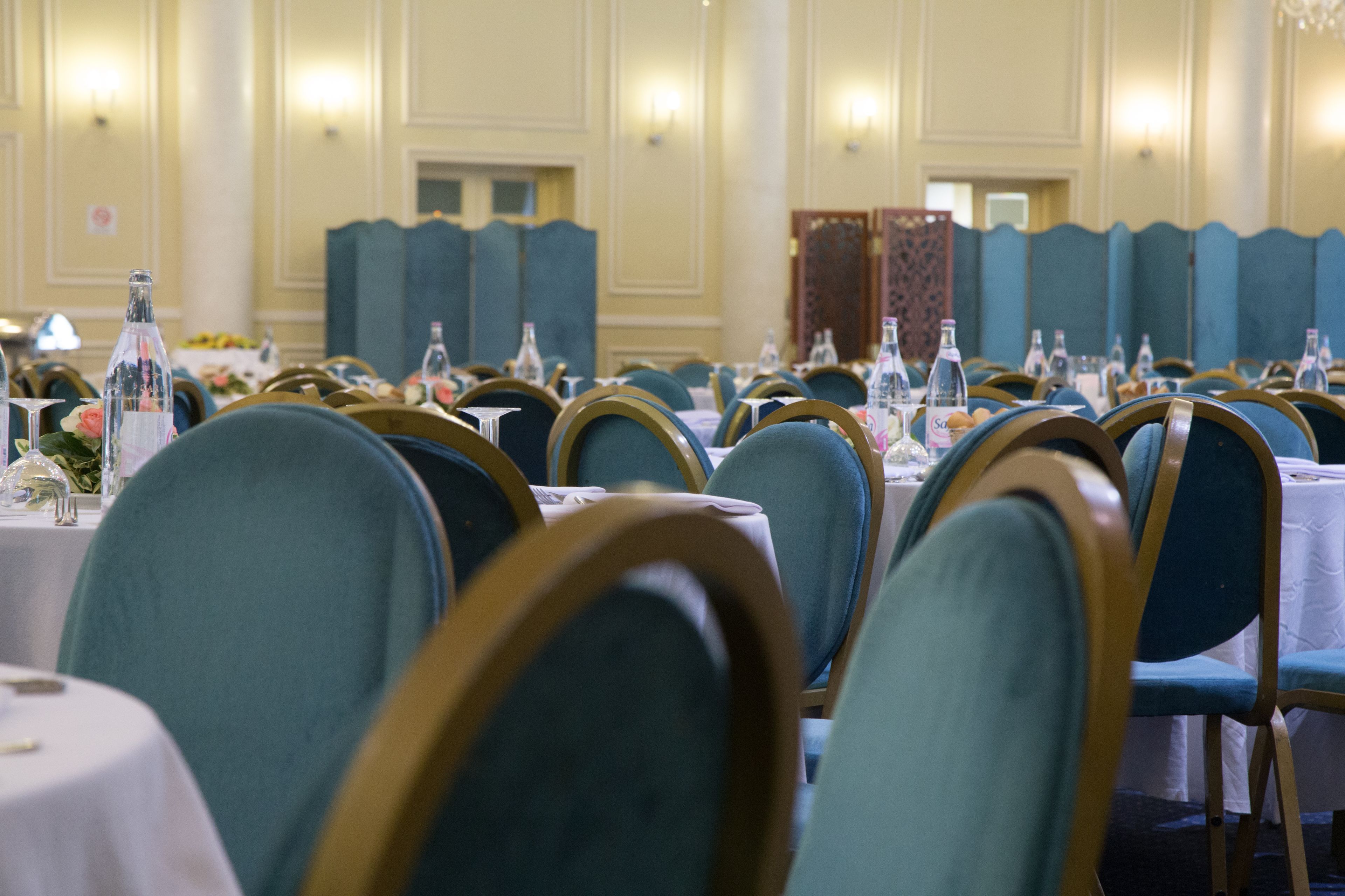 Une salle de banquet avec des rangées de tables, chacune étant agrémentée de chaises, de verres et de bouteilles.