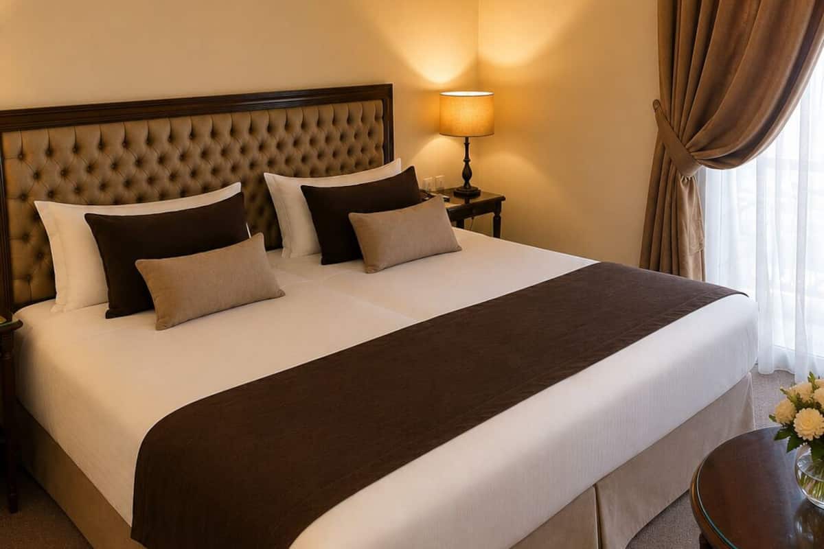 Habitación de hotel con una cama grande, una mesita de noche, una lámpara y vistas al exterior.