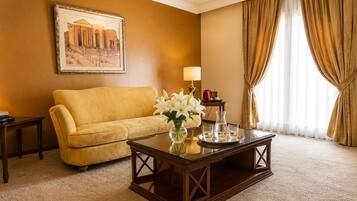 Habitación de hotel con sofá amarillo, una mesita de centro con un florero y una lámpara, además de un cuadro de ruinas antiguas en la pared.