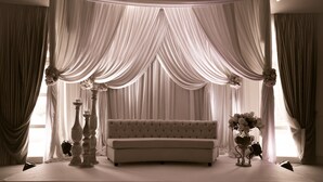 Una habitación con un sofá capitonado, cortinas drapeadas y arreglos florales.