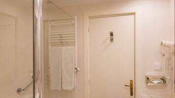 Un baño con ducha envuelta en vidrio, una puerta blanca, un lavabo con espejo y un secador de pelo en la pared.