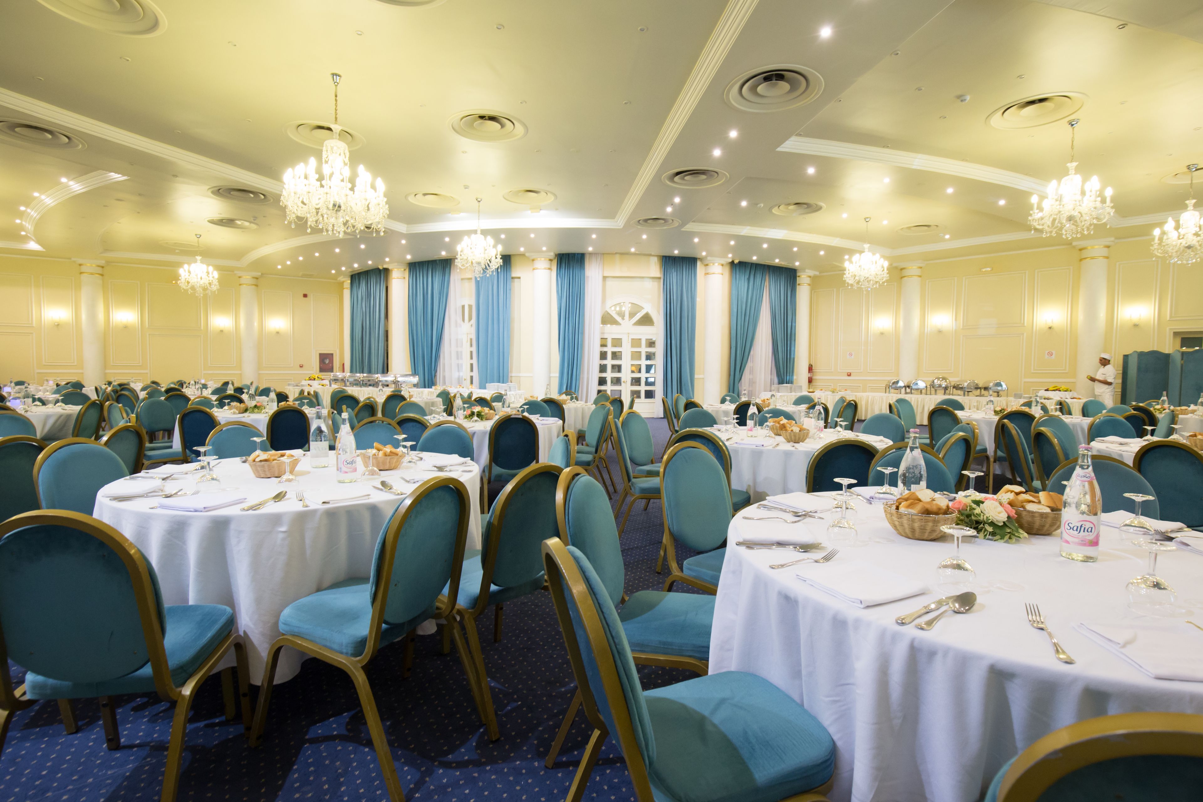 Un salón de banquetes con mesas redondas, sillas color turquesa y candelabros.