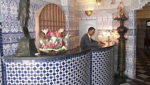Zona de recepción con pared de azulejos, una estatua, un arreglo floral y un mostrador con lámpara.