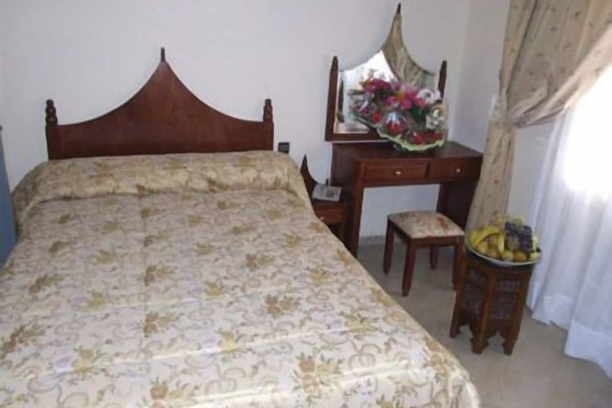 Un dormitorio con una cama, una mesita de noche de madera, un escritorio con un espejo y una silla.